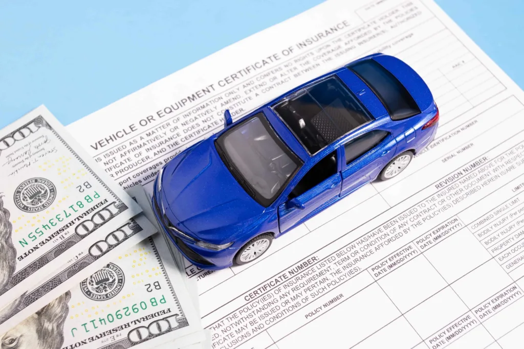 Blue toy car on vehicle insurance certificate with US dollar bills, symbolizing auto insurance coverage, policy documentation, and financial protection for car accidents.