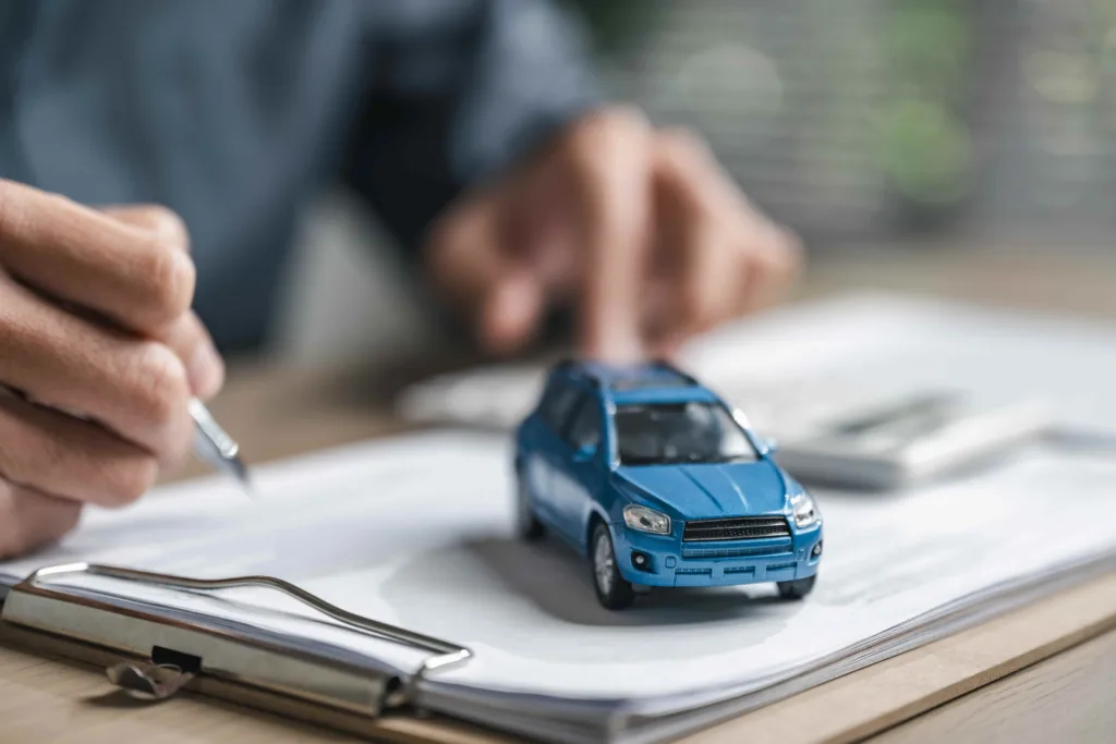 Person signing auto insurance paperwork with toy car on documents, representing vehicle insurance policy, coverage agreement, and car accident claim process.