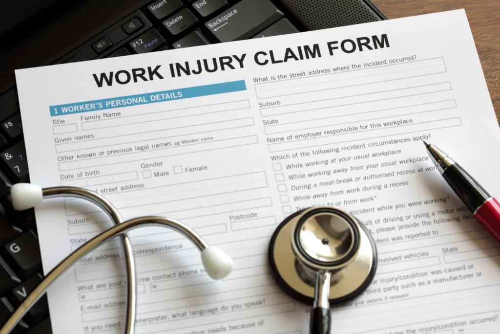 Work injury claim form on desk with stethoscope and pen, representing workers’ compensation paperwork.
