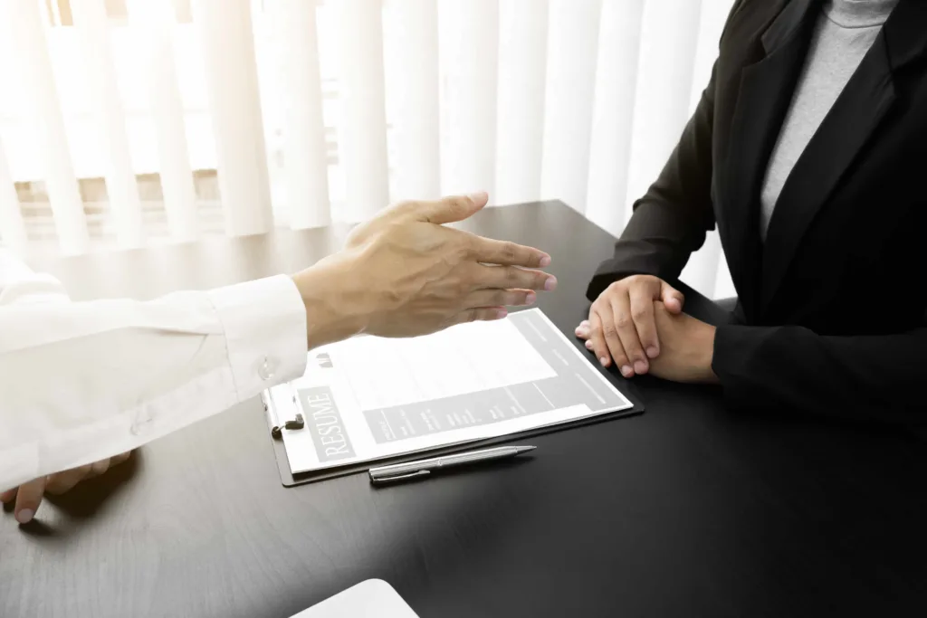 Job interview with hiring manager shaking hands with candidate over resume on office desk.