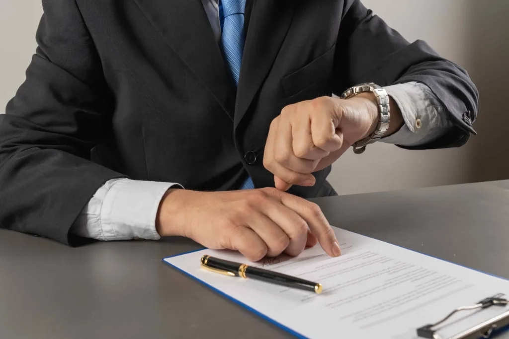 Businessman in suit checking time while reviewing and signing legal contract at desk.