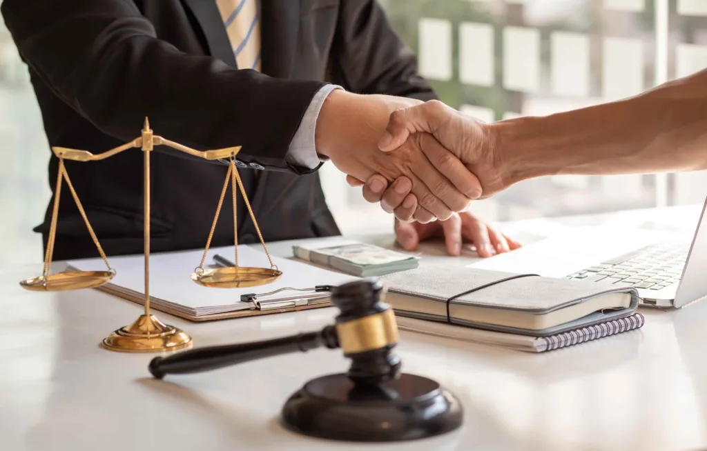 Lawyer and client shaking hands over legal documents with gavel and scales of justice, symbolizing successful legal settlement or agreement
