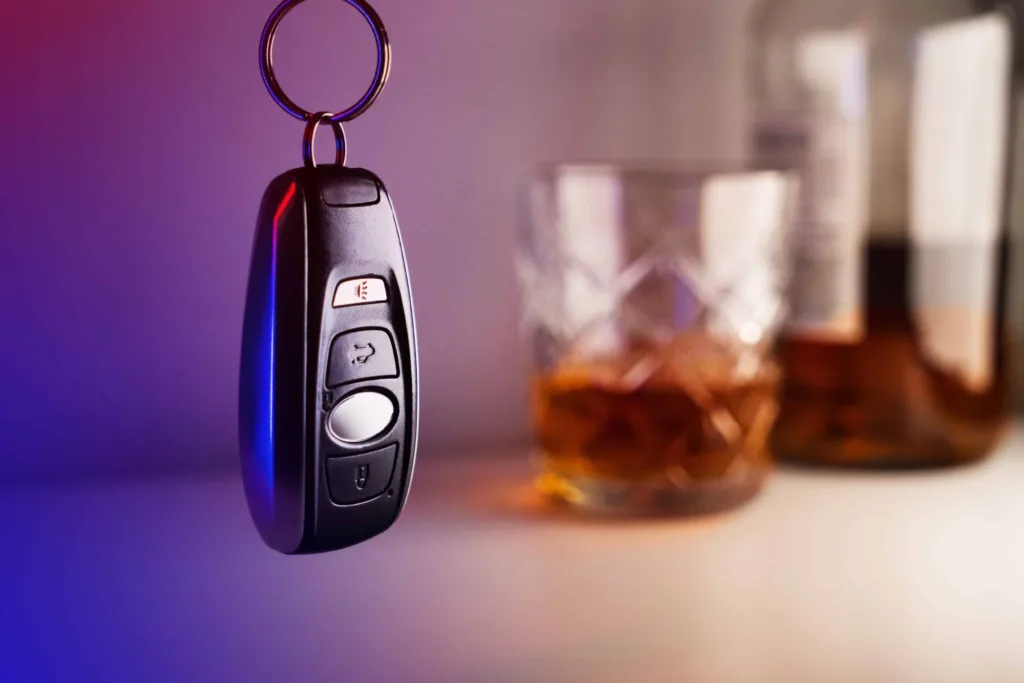 Car key fob with whiskey glass and bottle in background, representing drunk driving risk and DUI concept