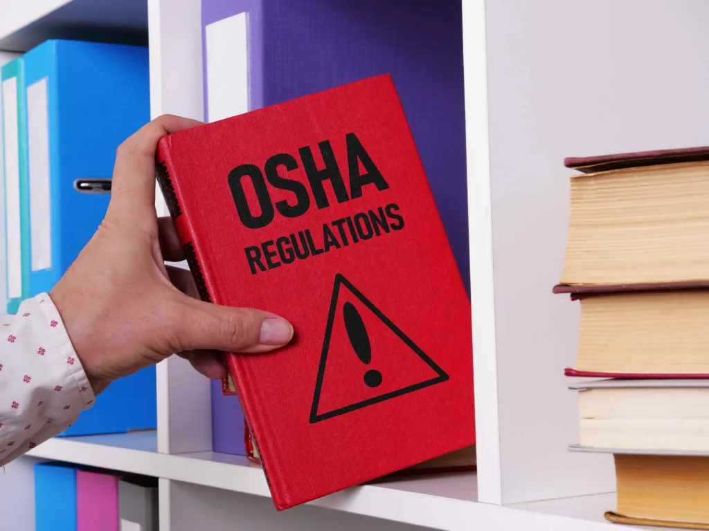 Hand pulling OSHA regulations book from shelf, workplace safety standards and compliance concept