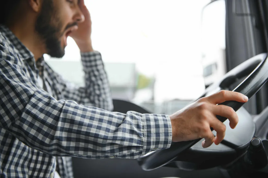 Fatigued truck driver rubbing his eyes behind the wheel